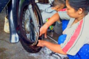 Istri tukang tambal ban ikut membantu suaminya menambal ban.